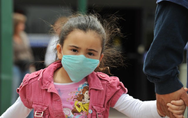 A girl, wearing a mask, holds her father's hand as they cross the international border between US and Mexico in San Ysidro, California, on April 27, 2009. The World Health Organization (WHO) raised its flu pandemic alert level from three to four, signalling a "significant increase in risk of a …