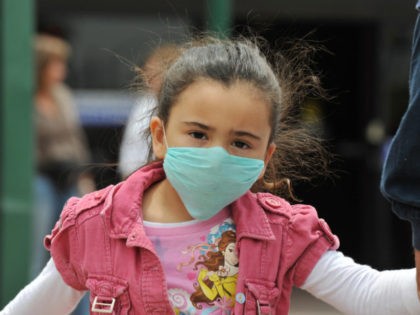 A girl, wearing a mask, holds her father's hand as they cross the international border bet