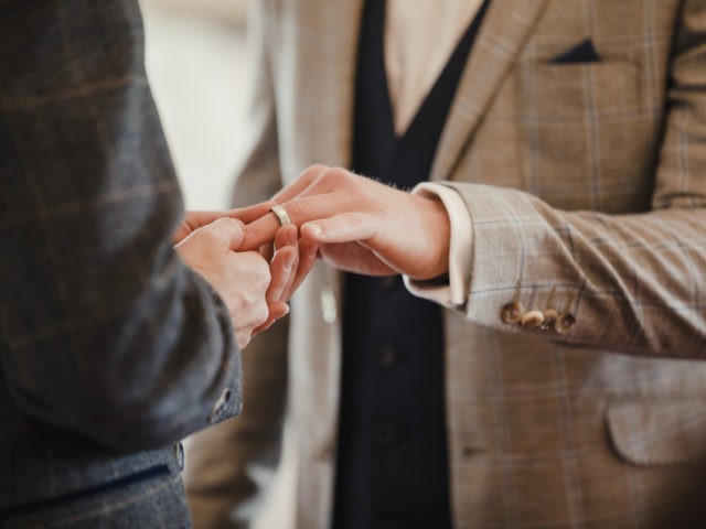 Two men are exchanging rings on their wedding day.