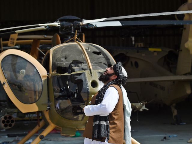 A Taliban member looks up standing next to a damaged helicopter at the airport in Kabul on