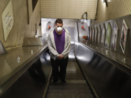 A man wearing a face mask travels up an escalator in a London Underground tube station in London on March 25, 2020, after Britain's government ordered a lockdown to slow the spread of the novel coronavirus. - Britain was under lockdown, its population joining around 1.7 billion people around the …