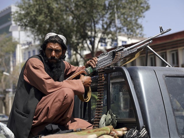 Taliban fighter sit on the back of vehicle with PK machine gun in front of main gate leadi