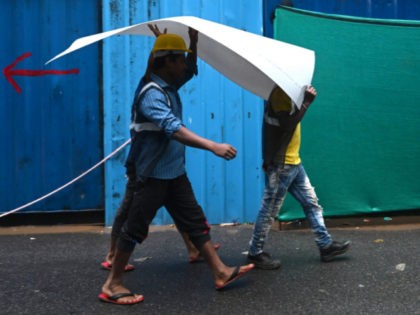 Construction workers use a plastic sheet to shelter during a rainfall in New Delhi on Sept