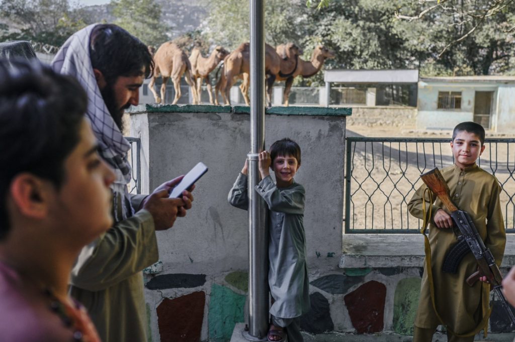 A boy poses for a picture with the rifle of a Taliban fighter near the camel enclosure at the Kabul zoo on September 17, 2021. (Bulent Kilic/AFP via Getty Images)