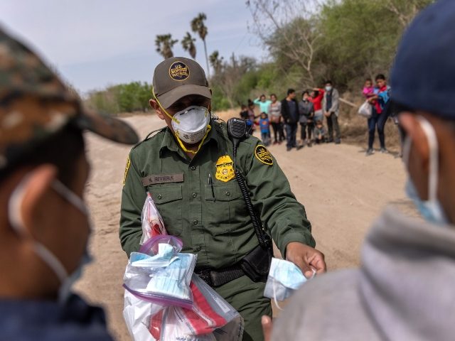 HIDALGO, TEXAS - MARCH 25: A U.S. Border Patrol agent hands out masks to unaccompanied minors after a group of asylum seekers crossed the-Rio Grande into Texas on March 25, 2021 in Hidalgo, Texas. A large group of families and unaccompanied minors, mostly teenagers, came across the border onto private …