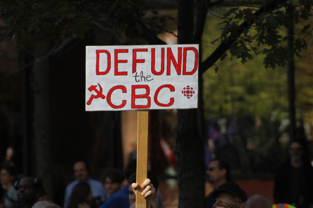 A protester holds a sign outside of CBC headquarters during a People’s Party of Canada (PPC) event. (Photo: Chris Tomlinson/Breitbart London)