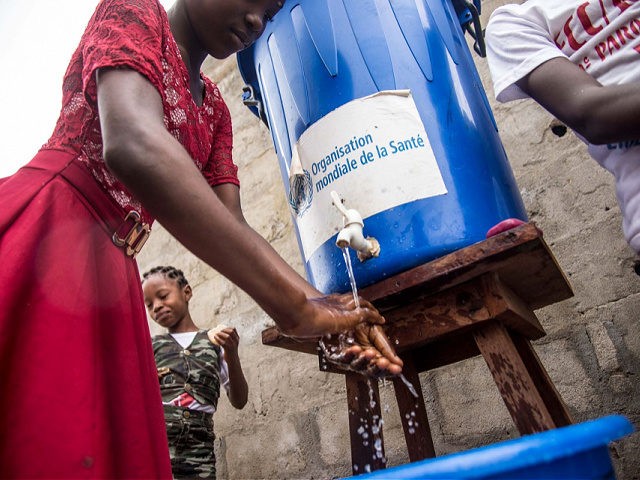 A woman washes her hands from a tank of water bearing a World Health Organization (WHO-OMS) sticker, as a prevention against Ebola virus after a Pentecost mass at the Church of Christ on May 20, 2018 in Mbandaka, northwest of DR Congo. - The Democratic Republic of Congo is preparing …