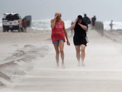 People shield their face from wind and sand ahead of Tropical Storm Nicholas, Monday, Sept. 13, 2021, on the North Packery Channel Jetty in Corpus Christi, Texas. Lifeguards paroled the beach to warn people of the upcoming conditions.