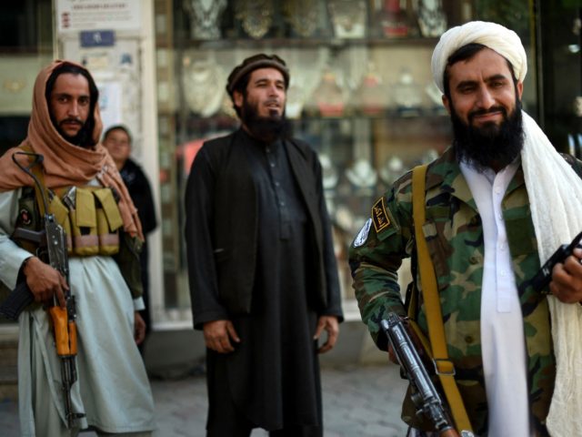 Taliban fighters stand guard on the backdrop of shops selling antiques and decorative merc