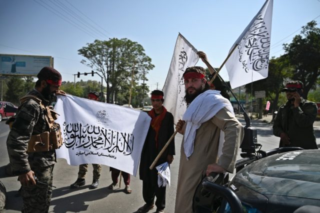 Taliban fighters holding the group's flag stand guard along a road in Kabul
