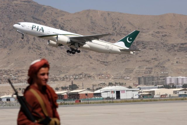 A Taliban fighter stands guard as a Pakistan International Airlines plane takes off from K