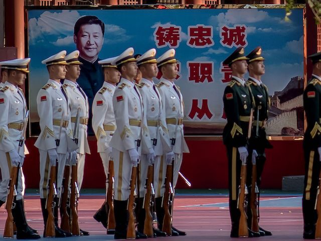 Military personnel stand in formation next to a portrait of China's President Xi Jinping (