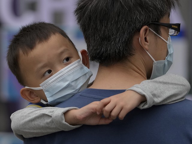 A man carries a child, both wearing face masks to help curb the spread of the coronavirus, walk on a street in Beijing, September 12, 2021. (AP Photo/Andy Wong)