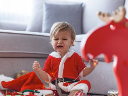 Crying Santa baby boy. Cute baby boy wearing Christmas clothes at home. Merry Christmas. H