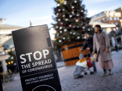 Pedestrians wearing a protective face covering to combat the spread of the coronavirus, pass COVID-19 information sign reading "STOP the spread" as they walk past a Christmas tree in Covent Garden in central London, on November 22, 2020, as the four-week national shutdown imposed in England continues, forcing people to …