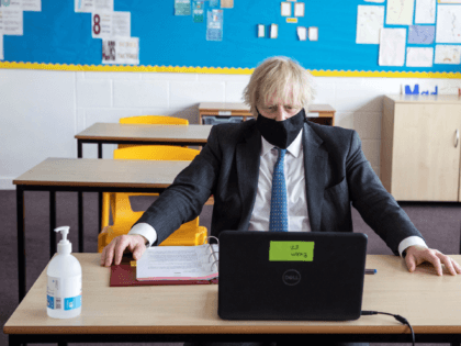 Britain's Prime Minister Boris Johnson, wearing a face covering, sits in front of a laptop