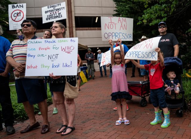 People hold up signs during a rally against "critical race theory" (CRT) being taught in schools at the Loudoun County Government center in Leesburg, Virginia on June 12, 2021. - "Are you ready to take back our schools?" Republican activist Patti Menders shouted at a rally opposing anti-racism teaching that …
