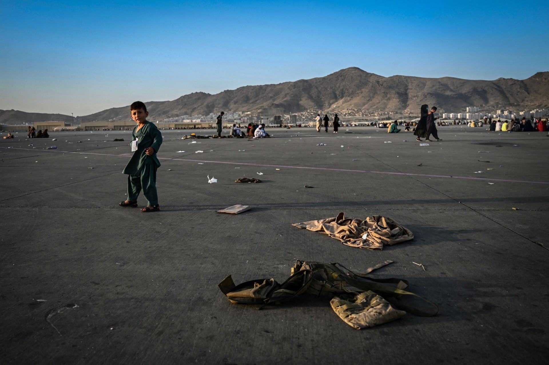TOPSHOT - An Afghan child walks near military uniforms as he with elders wait to leave the Kabul airport in Kabul on August 16, 2021, after a stunningly swift end to Afghanistan's 20-year war, as thousands of people mobbed the city's airport trying to flee the group's feared hardline brand of Islamist rule. (Photo by Wakil Kohsar / AFP) (Photo by WAKIL KOHSAR/AFP via Getty Images)