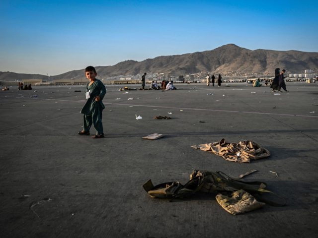 TOPSHOT - An Afghan child walks near military uniforms as he with elders wait to leave the Kabul airport in Kabul on August 16, 2021, after a stunningly swift end to Afghanistan's 20-year war, as thousands of people mobbed the city's airport trying to flee the group's feared hardline brand …