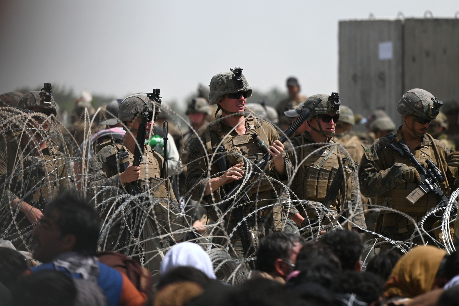 US soldiers stand guard behind barbed wire as Afghans sit on a street near the military wing of the airport in Kabul on August 20, 2021, hoping to leave the country after the Taliban took over Afghanistan.  (Photo by Wakil KOHSAR/AFP) (Photo by WAKIL KOHSAR/AFP via Getty Images)