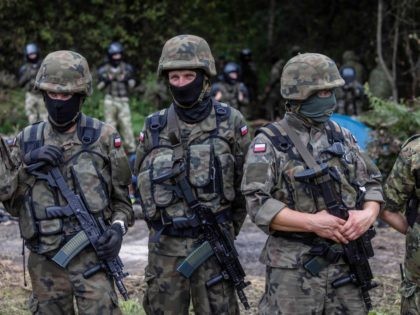 Polish soldiers and border guards stand next to migrants believed to be from Afghanistan in the small vilage of Usnarz Gorny near Bialystok, northeastern Poland, located close to the border with Belarus, on August 20, 2021. - The fate of 32 migrants stranded on the border between Belarus and Poland …