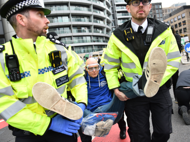 A climate activist from the group Insulate Britain is arrested and carried away by police during a demonstration in which they blocked a round about calling for the UK government to fund the insulation of Britain's homes in central London on October 8, 2021. - Climate activist group Insulate Britain …