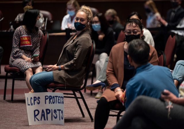 A woman sits with her sign during a Loudoun County Public Schools (LCPS) board meeting in Ashburn, Virginia on October 12, 2021. - Loudoun county school board meetings have become tense recently with parents clashing with board members over transgender issues, the teaching of critical race theory (CRT) and Covid-19 …