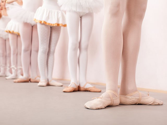 Group of six little ballerinas standing in row behing their ballet teacher and practicing