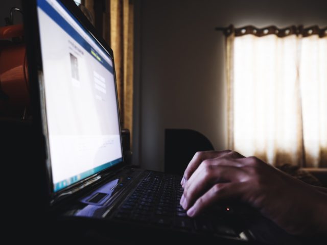 Hand typing laptop computer keypad, in dark room, selective focus