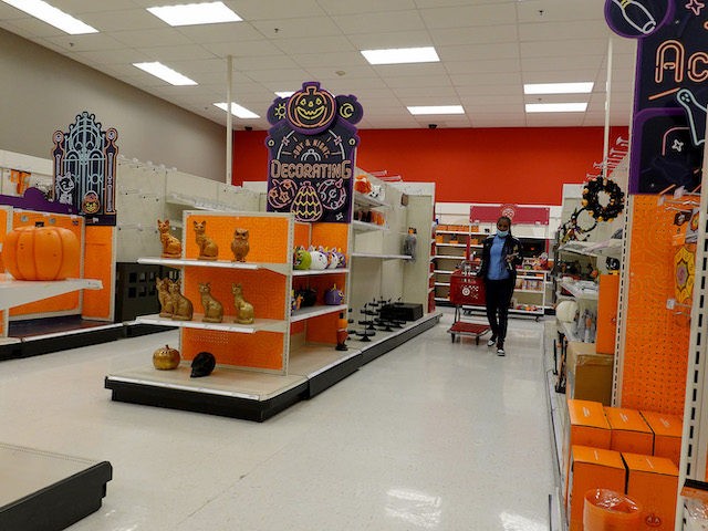 A shopper walks past shelves with only a few items in the Halloween section in a Target st