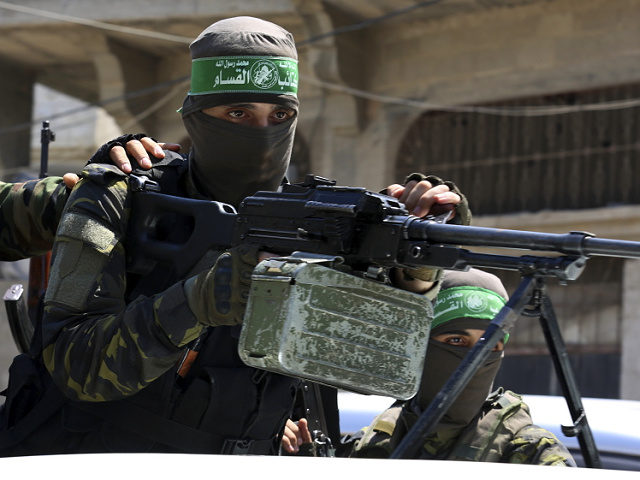 A masked militant from the Izzedine al-Qassam Brigades, a military wing of Hamas, stands behind a machine gun on a truck as mourners carry the body of Osama Dueij, 32, who was shot in the leg on Saturday during a violent demonstration on the northern border between Gaza and Israel, …