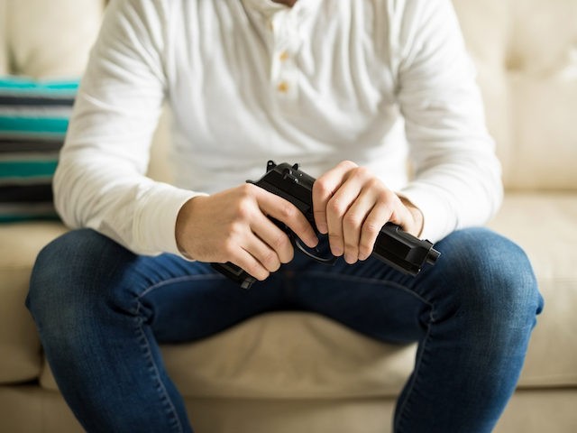 Close up of man with a pistol in hand sitting on couch (Stock Photo/Getty Images)