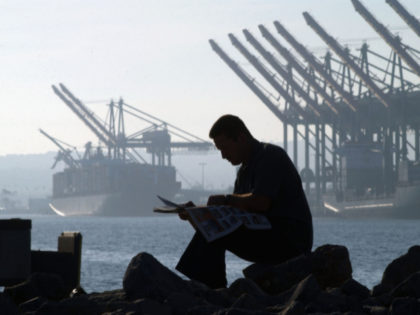 LOS ANGELES, CA - OCTOBER 9: A trucker reads a newspaper near ships and cranes as he waits