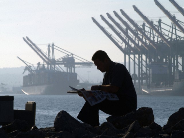 LOS ANGELES, CA - OCTOBER 9: A trucker reads a newspaper near ships and cranes as he waits for the re-opening of the Port of Los Angeles on October 9, 2002 in Los Angeles, California. President George W. Bush used a court order to force the opening of West Coast ports tonight, ending an estimated $1 billion-per-day loss to the United States economy. (Photo by David McNew/Getty Images)