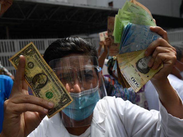 A health worker wearing a face mask and shield holds a one dollar bill in one hand and its