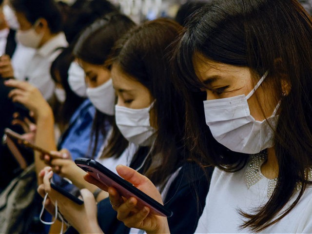People wearing face masks check their phones on the subway in Osaka on August 17, 2021. (P