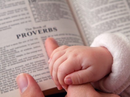 Baby holding father’s finger as he points to Proverbs verse