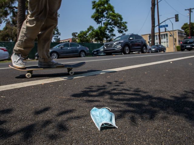 A man rides his skateboard next to a discarded face mask on the street in Long Beach, California on August 22, 2020. - Due to the novel coronavirus, COVID-19, more people wear masks to prevent the spread, more personal protective equipment, or PPE, has been found as litter around the …