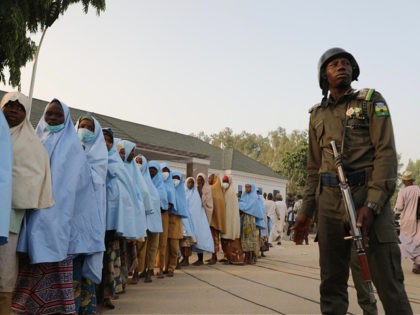 TOPSHOT - A soldiers stands next to a group of girls previously kidnapped from their boarding school in northern Nigeria are seen on March 2, 2021 at the Government House in Gusau, Zamfara State upon their release. - All 279 girls kidnapped from their boarding school in northern Nigeria have …