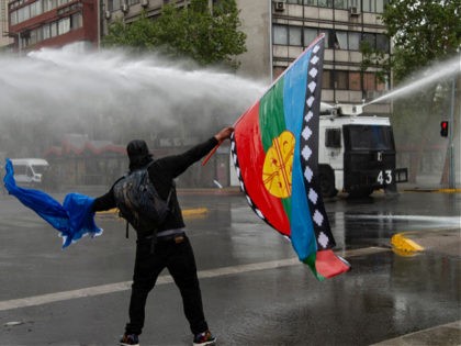 A man holds a Mapuche indigenous flag as he confronts riot police during clashes in downtown Santiago, on October 10, 2021, amid the commemoration of the Day of the Race. (Photo by Martin BERNETTI / AFP) (Photo by MARTIN BERNETTI/AFP via Getty Images)