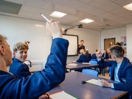 Point of view shot of a high school lesson where the teacher has asked a question and some students have their hands up to answer.
