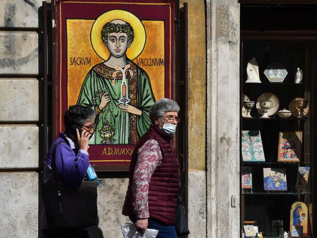 Pedestrians walk past a poster designed and displayed overnight by Italian street artist Mauro Pallotta, aka Maupal, on October 1, 2020 in the Borgo Pio district of Rome near The Vatican, inspired by an icon of St. Stephen, representing the Saint holding a hypodermic syringe of vaccine and reading in …