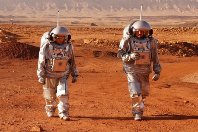 A couple of trainee astronauts walk in their spacesuits during a training mission for plan