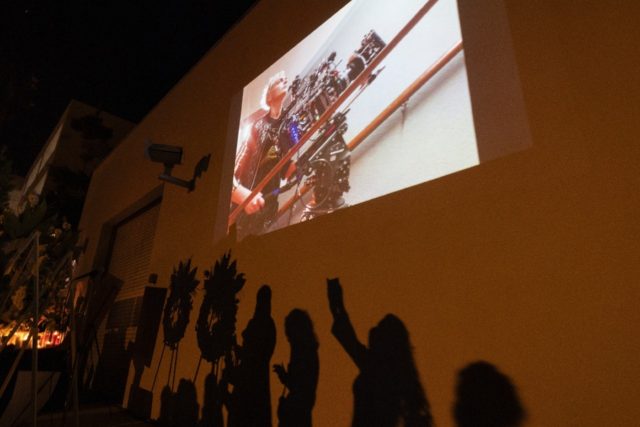 A photo of cinematographer Halyna Hutchins is seen above the shadows of people approaching