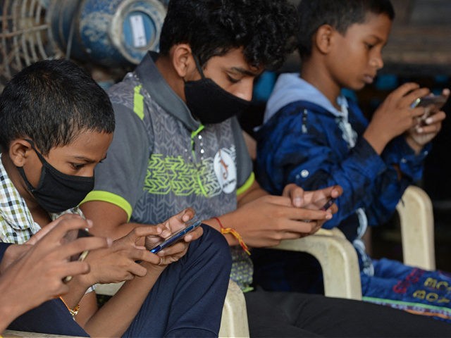 Children play games on their mobile phones at a street corner in Mumbai on September 6, 20