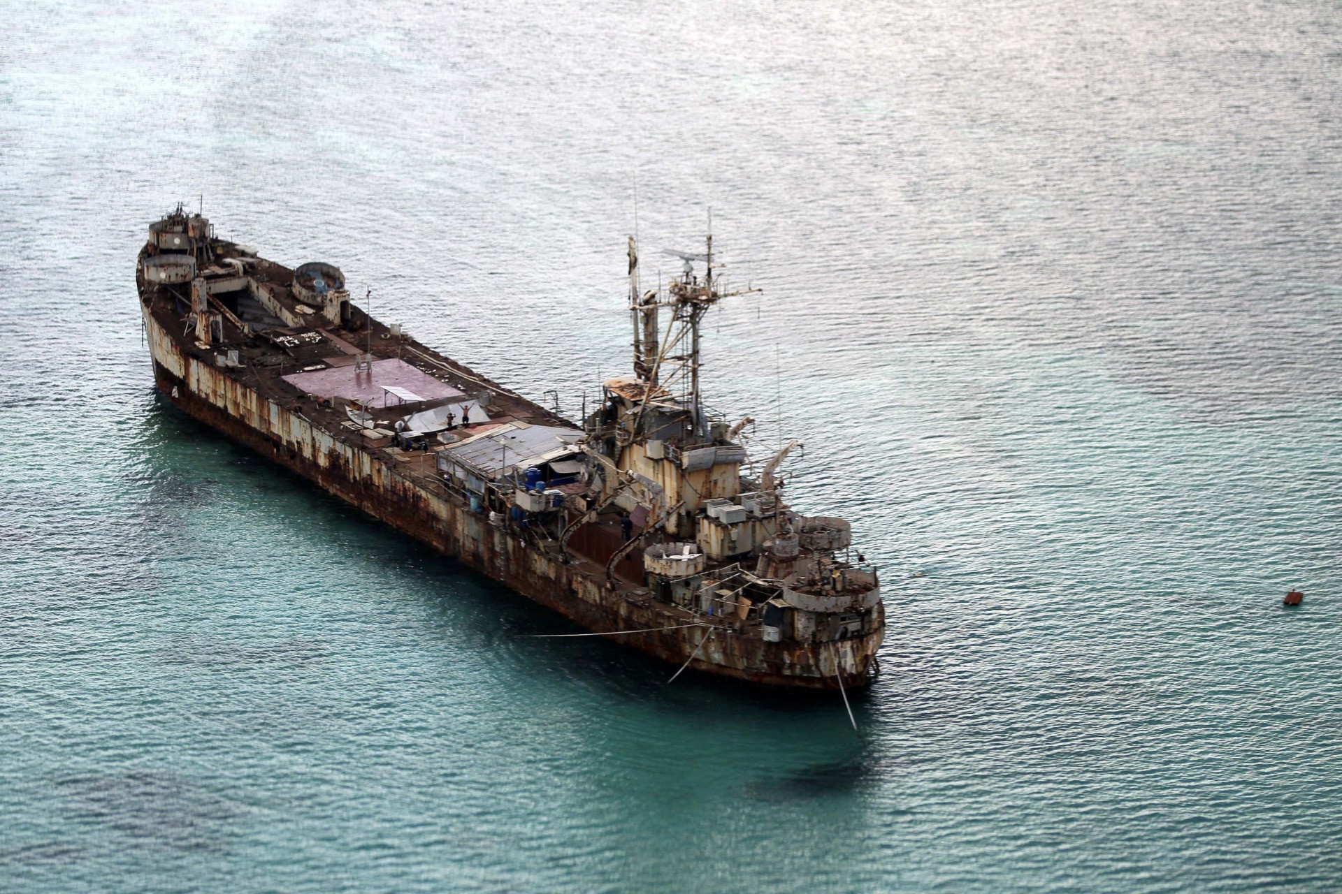 This areral photo taken through a glass window of a military plane shows the dilapidated Sierra Madre ship of the Philippine Navy anchored near Ayungin Shoal with Filipino soldiers onboard to secure perimeter in the Spratly Islands in the South China Sea on May 11, 2015. Chinese coast guard ships blocked and used water cannons on two Philippine supply boats heading to a disputed shoal occupied by Filipino marines in the South China Sea, provoking an angry protest against China and a warning from the Philippine government that its vessels are covered under a mutual defense treaty with the U.S., Manila’s top diplomat said Thursday, Nov. 18, 2021. (Ritchie B. Tongo/Pool Photo via AP, File)