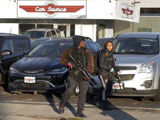 Erick Jordan and his daughter Jade, 16, carrying rifles, stand at the Car Source while protesters march, Sunday, Nov. 21, 2021 in Kenosha, Wis. Kyle Rittenhouse was acquitted of all charges after pleading self-defense in the deadly Kenosha shootings that became a flashpoint in the nation's debate over guns, vigilantism and racial injustice. (AP Photo/Paul Sancya)