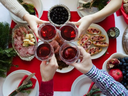 Flat-lay of friends hands toasting with glasses of red wine. Family gathering concept. Traditional Italian Christmas dinner food - lentils with Cotechino, antipasti, Panettone and fruits. Top view.