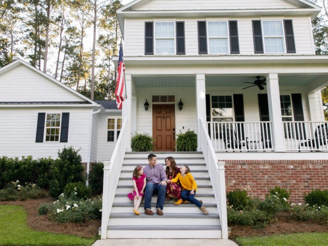 Family sitting outside on the steps of a new construction white siding farmhouse in the su