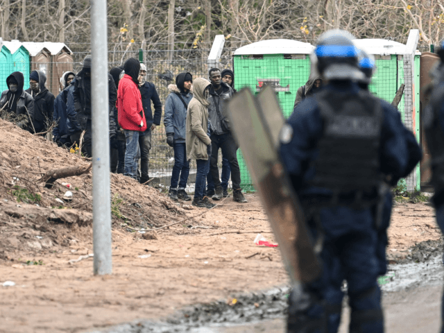 Police stand next to migrants at the makeshift camp in Calais, northern France, on November 28, 2019 following clashes between migrants. - At least five migrants, from Ethiopia and Sudan, have been injured during clashes on November 28, 2019. (Photo by DENIS CHARLET / AFP) (Photo by DENIS CHARLET/AFP via …
